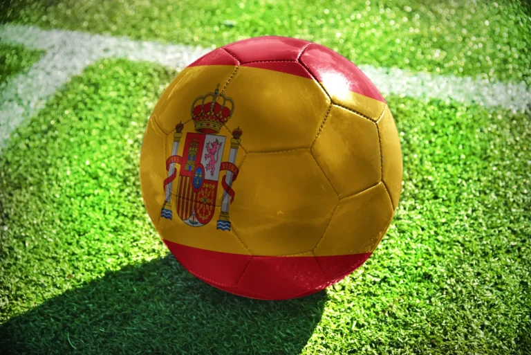 football ball with the national flag of spain lies on the green field near the white line